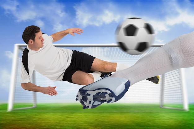 Imagen compuesta de jugadores de fútbol que luchan por el balón con calcetines y botas contra el campo de fútbol y el gol bajo un cielo azul