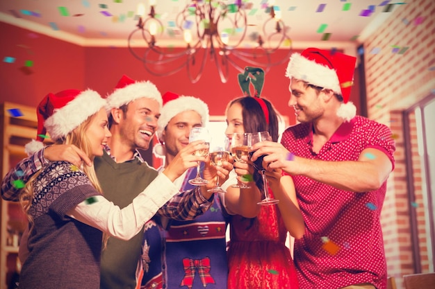 Imagen compuesta de lindo grupo de amigos brindando con gorros de Papá Noel