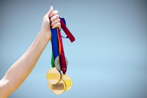 Foto imagen compuesta de mano sujetando medallas sobre fondo blanco.