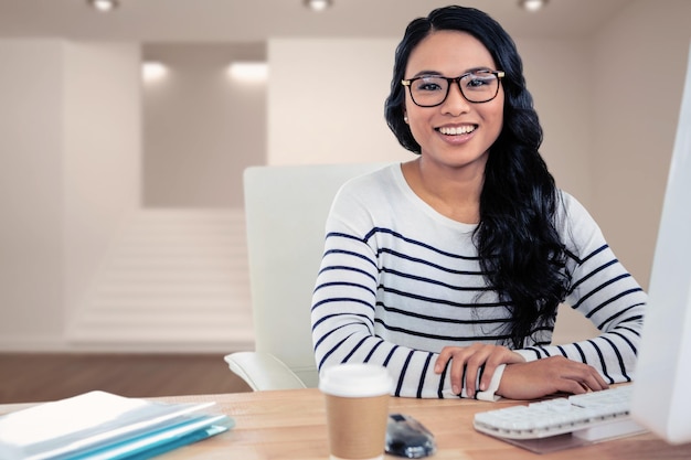 Imagen compuesta de mujer asiática sonriente sentada en el escritorio posando para la cámara