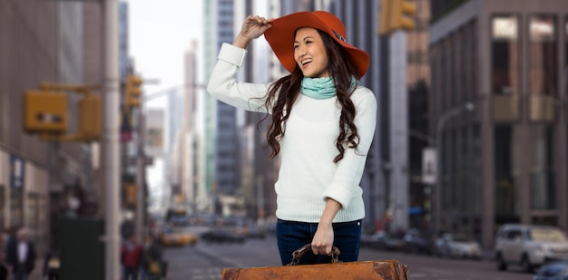 Imagen compuesta de mujer asiática sonriente sosteniendo equipaje sosteniendo sombrero