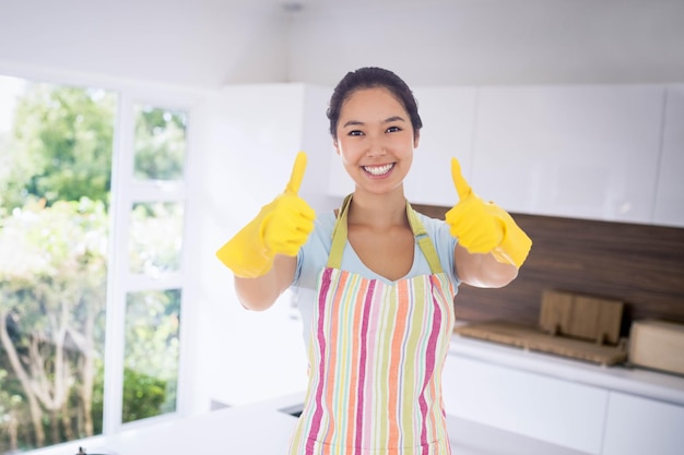 Imagen compuesta de mujer feliz dando Thumbs up en guantes de goma