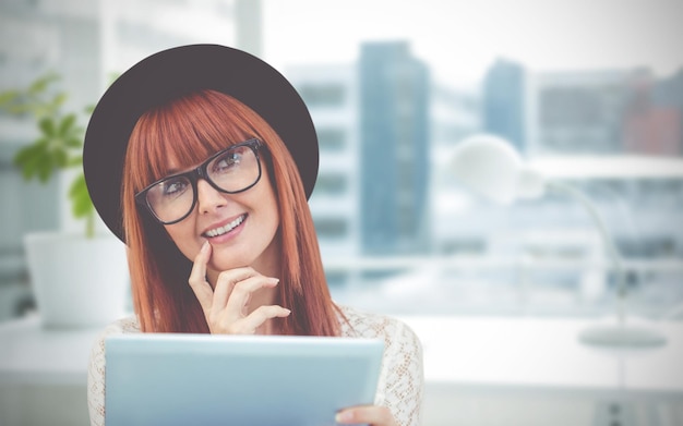Imagen compuesta de mujer hipster sonriente usando su tableta