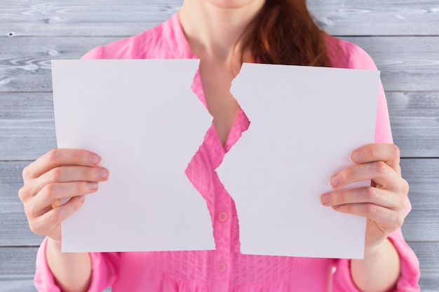 Imagen compuesta de mujer sosteniendo una hoja de papel rasgada