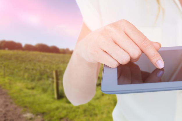 Imagen compuesta de mujer con tablet pc contra el paisaje rural