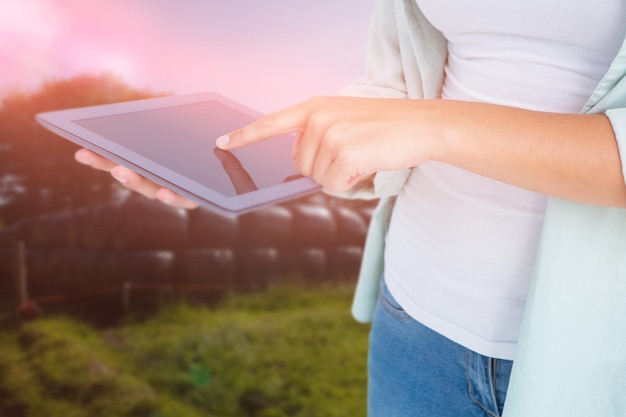 Imagen compuesta de mujer con tablet pc contra el paisaje rural