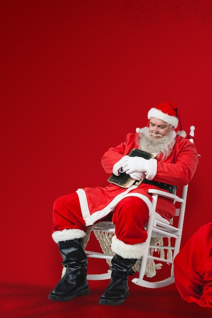 Foto imagen compuesta de santa claus sosteniendo la biblia mientras duerme la siesta en la silla