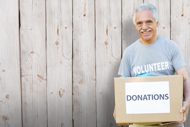 Imagen compuesta de senior voluntario feliz celebración caja de donación