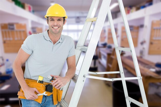 Imagen compuesta de trabajador sosteniendo herramientas mientras se apoya en la escalera