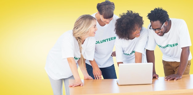 Imagen compuesta de voluntarios sonrientes que trabajan juntos en una computadora portátil