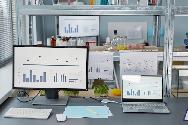 Imagen de computadoras con gráficos en la pantalla y tubos de ensayo con muestras en los estantes para experimentos científicos en el laboratorio