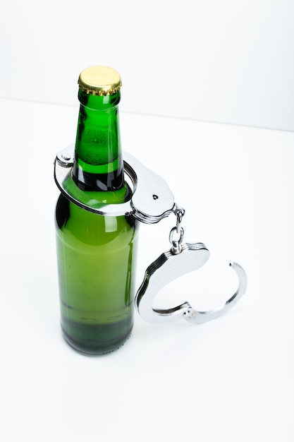 Imagen conceptual de beber ilegalmente con una botella de cerveza y un par de esposas