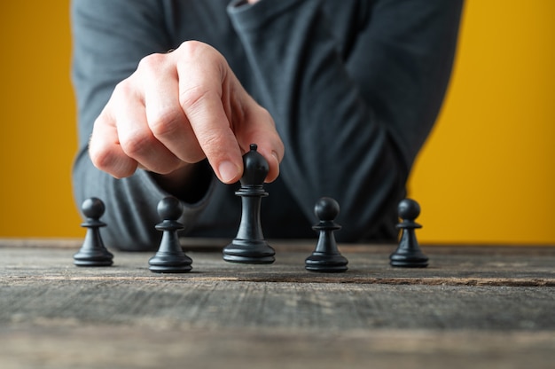 Imagen conceptual de la estrategia y el poder con la mano masculina posicionamiento de piezas de ajedrez sobre tablero de madera rústica.