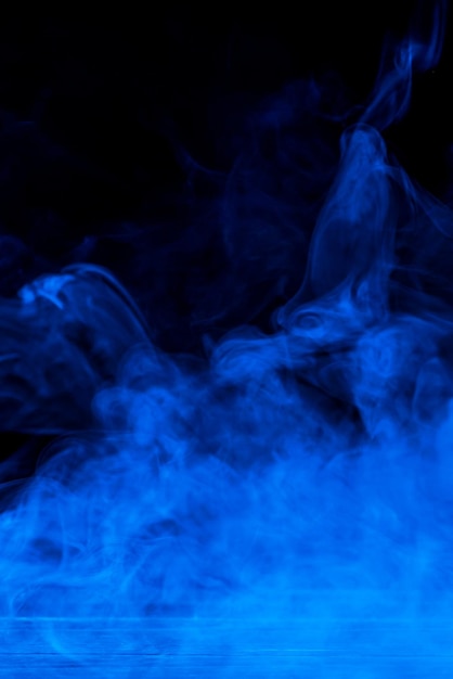 Imagen conceptual de humo azul aislado sobre fondo negro oscuro y mesa de madera