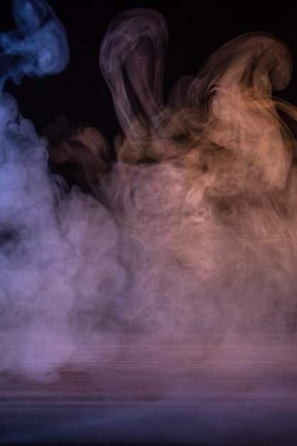 Foto imagen conceptual de humo multicolor aislado sobre fondo negro oscuro y mesa de madera