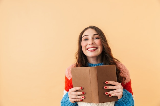 Imagen de contenido mujer de 20 años con cabello largo sonriendo y leyendo un libro, que se encuentran aisladas