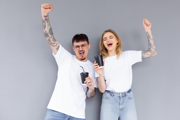 Imagen de contenido pareja hombre y mujer en ropa de mezclilla sonriendo mientras sostiene tazas de café para llevar