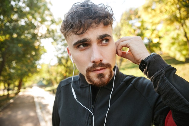 Imagen de corredor de hombre de fitness deportivo joven guapo al aire libre en el parque escuchando música con auriculares.