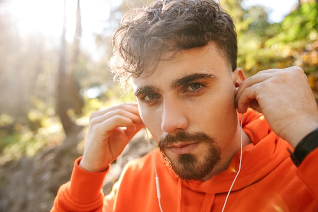 Imagen de corredor de hombre de fitness deportivo joven guapo al aire libre en el parque escuchando música con auriculares.