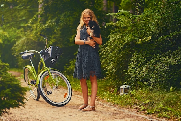 La imagen de cuerpo completo de la chica rubia sostiene al perro Spitz sobre el fondo de la bicicleta.