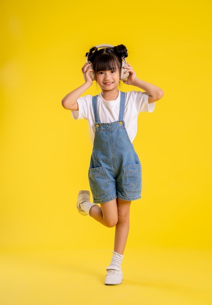 Imagen de cuerpo completo de niña asiática posando sobre un fondo amarillo