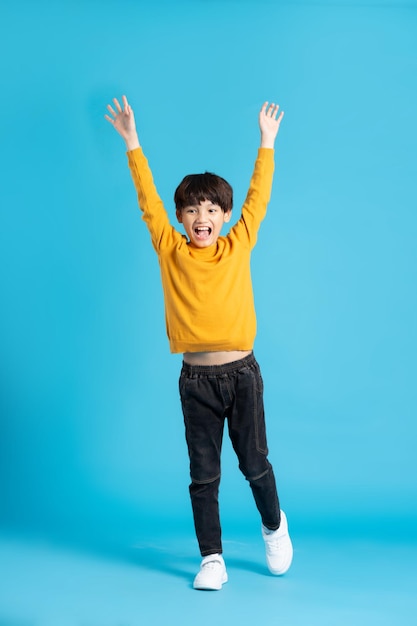 Imagen de cuerpo completo del niño asiático posando sobre fondo azul.