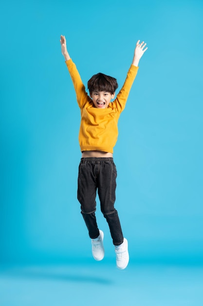 Imagen de cuerpo completo del niño asiático posando sobre fondo azul.