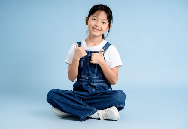 Imagen de cuerpo entero de una chica asiática sentada y posando sobre un fondo azul