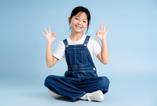 Imagen de cuerpo entero de una chica asiática sentada y posando sobre un fondo azul
