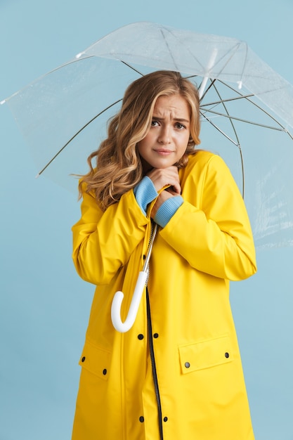 Imagen de cuerpo entero de una elegante mujer de 20 años con impermeable amarillo de pie bajo un paraguas transparente