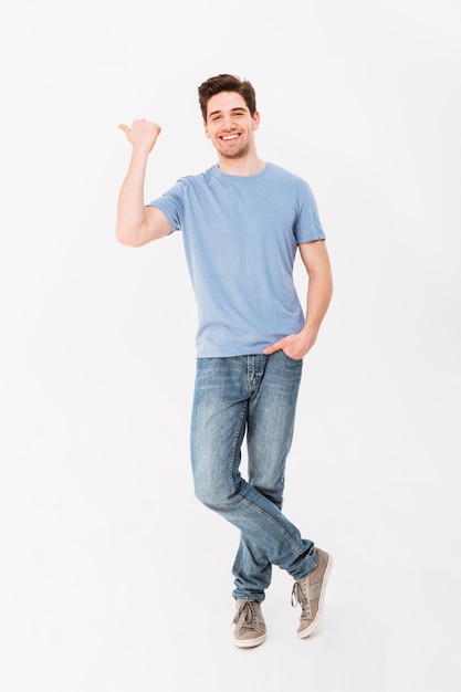 Imagen de cuerpo entero del hombre guapo regocijándose y señalando con el dedo a un lado en copyspace, aislado sobre la pared blanca