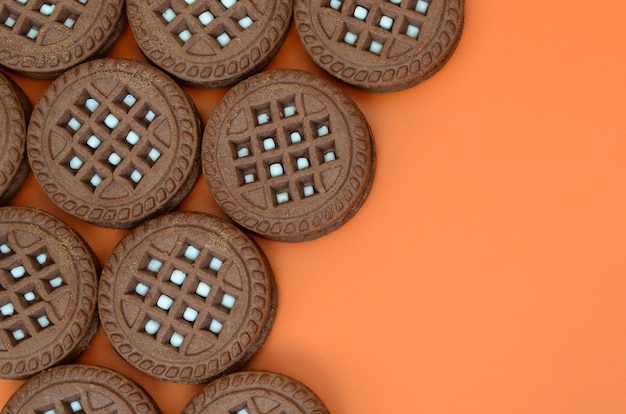 Imagen detallada de las galletas redondas del bocadillo del marrón oscuro con el coco que llena en una superficie anaranjada. Imagen de fondo de un primer plano de varias golosinas para el té