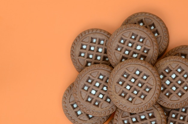 Imagen detallada de las galletas redondas del bocadillo del marrón oscuro con el coco que llena en una superficie anaranjada.