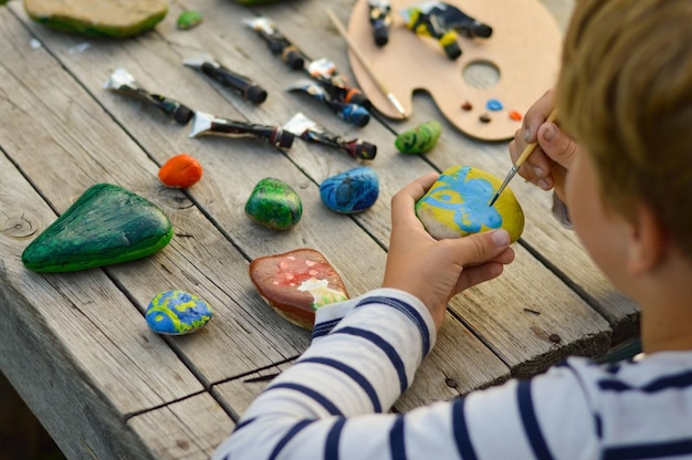 Una imagen detallada de las manos de un niño dibujando un hongo en una piedra con pinturas acrílicas Los pasatiempos domésticos son auténticos Obras de arte en piedras