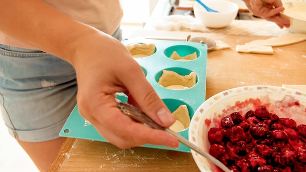 Imagen de detalle de mujer joven poniendo salsa de bayas frescas en cupcakes. Mujer horneando pasteles y tartas en casa