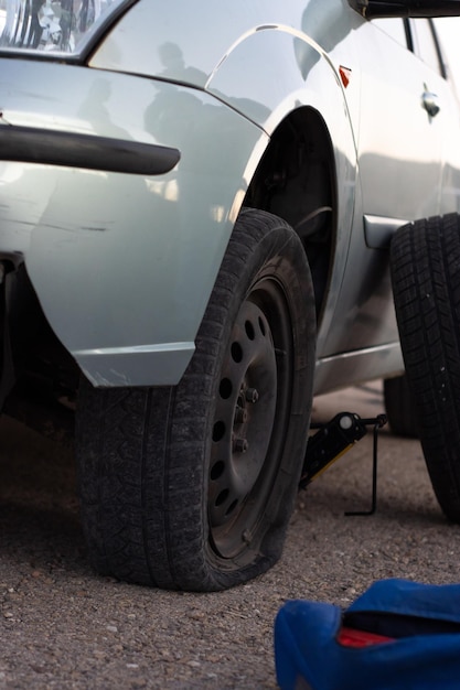 Imagen de detalle vertical de un automóvil con una llanta pinchada a punto de cambiar la llanta