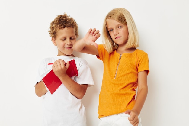 Imagen de diversión positiva de niño y niña en camisetas coloridas con un fondo aislado de bloc de notas inalterado