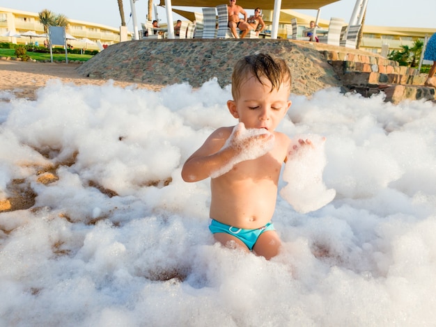 Imagen divertida del niño pequeño cubierto de jabón divertido en la fiesta de discoteca de la playa del mar