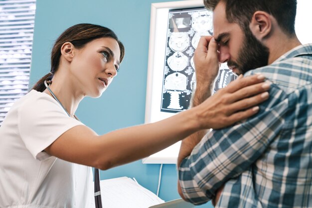 Imagen de una doctora en uniforme médico y un paciente frustrado mirando los resultados de la tomografía computarizada de rayos X en el hospital