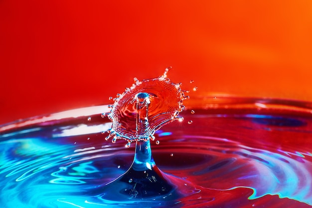 Imagen de dos gotas de agua chocando sobre el agua azul con fondo rojo.