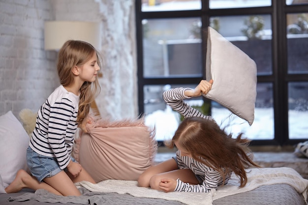 La imagen de dos hermanitas sentadas en la cama en la habitación en la que usan la almohada para pelear entre sí.