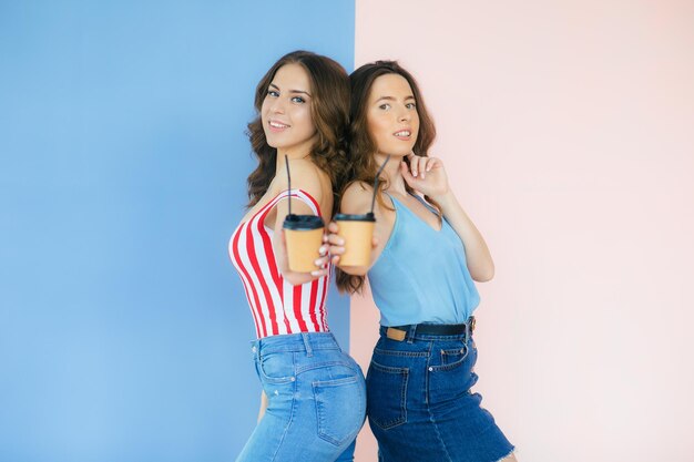 Foto imagen de dos mujeres felices sosteniendo café para llevar en vasos de papel aislado sobre fondo de color
