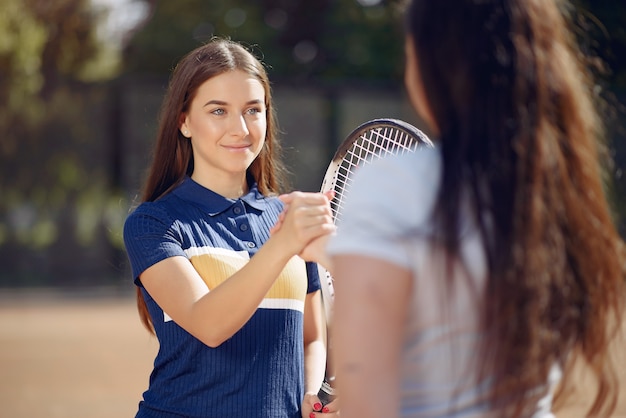 Imagen de dos mujeres que sacuden sus manos mientras juegan al tenis en la cancha de tenis al aire libre