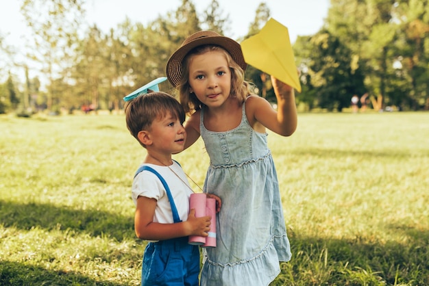 Imagen de dos niños jugando con binoculares y un avión de papel en un día de verano en el parque Hermana y hermano felices jugando al juego de safari al aire libre en el bosque Concepto de infancia