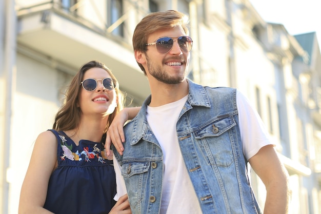 Imagen de la encantadora pareja feliz en ropa de verano sonriendo y cogidos de la mano juntos mientras camina por las calles de la ciudad.