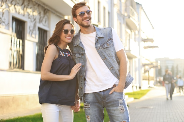 Imagen de la encantadora pareja feliz en ropa de verano sonriendo y cogidos de la mano juntos mientras camina por las calles de la ciudad.