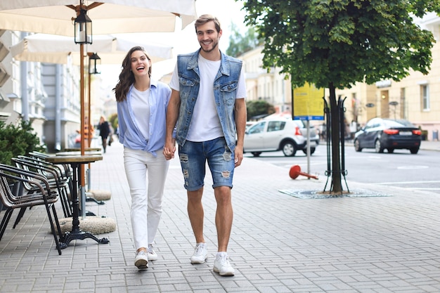 Imagen de la encantadora pareja feliz en ropa de verano sonriendo y cogidos de la mano juntos mientras camina por las calles de la ciudad.