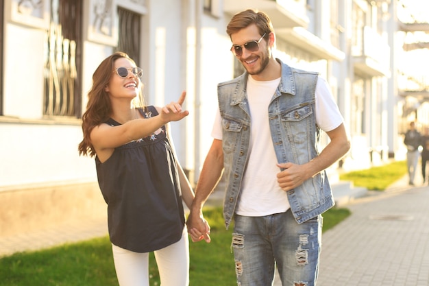 Imagen de la encantadora pareja feliz en ropa de verano sonriendo y cogidos de la mano juntos mientras camina por las calles de la ciudad.