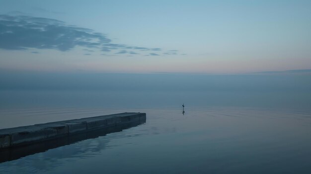 Foto la imagen es un largo muelle de hormigón que sobresale en un lago tranquilo el agua está quieta y refleja el cielo que es un gradiente de azul y rosa