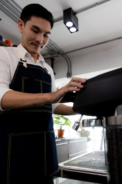 La imagen es retrato. Joven asiático con una máquina de café enjuague el café con agua tibia. Un hombre que se prepara para presionar el café molido para preparar espresso o americano en una cafetería.